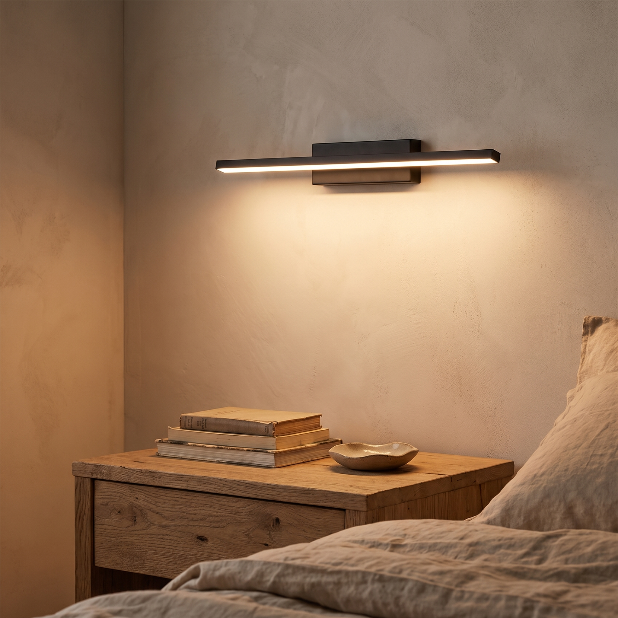 Black sconce lit above a bedside table
